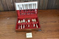 Full view of open wooden storage box lined with red velvet and white satin, displaying the Tudor Plate silverware set. Various knives, forks, spoons, and butter utensils are organized in their slots.