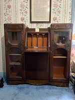 Front view of antique wooden desk with drop-front opened, showing interior compartments and both side cabinets with glass panes; left side missing one pane.