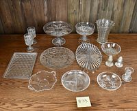 Wide view of the entire crystal glassware collection on wooden surface showing all trays, platters, bowls, glasses, vase, shakers, and candleholder.