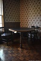 Octagonal dark wood poker table with leather top, showing shape and table legs in room corner with floral wallpaper and parquet floor.