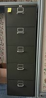 Full frontal view of the tall grey metal filing cabinet with five drawers, each with metal handles and label holders.