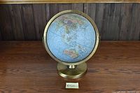 Globe displaying world map from the perspective showing Asia, Australia, and surrounding oceans, mounted on brass-colored base and ring.