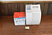 White Honeywell air purifier next to a box of Honeywell replacement pre-filters against a wood-paneled background.