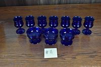 Seven cobalt blue wine glasses and three cobalt blue dessert bowls arranged in two rows on a wooden table.