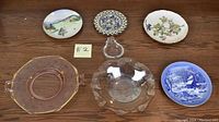 Photo showing six miscellaneous dishware items including three decorative plates and three serving bowls/dishes on a wooden surface.