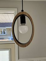 Front view of the modern hanging pendant light showing the wooden oval frame, bulb holder and clear bulb.