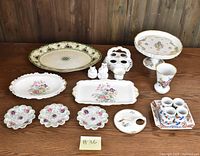 Photo showing an assortment of ceramic and porcelain tableware including trays, plates, egg holder, animal salt and pepper shakers, napkin rings, and a cup all with floral designs.
