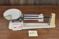 OHAUS triple beam balance scale on wooden table showing overall condition and details of sliding weights and weighing pan.