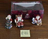 Three Royal Albert Christmas figurines displayed in front of a Royal Albert decorated box.