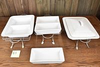 Four white ceramic serving platters, three with metal stands, displayed on a wooden surface.