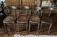 Four wooden chairs arranged side by side showing front view, wood grain and wear
