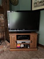 43-inch Sylvania flat-screen TV sitting on a wooden stand with closed brick wall to the left and framed paintings on the wall behind.