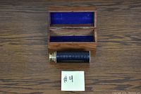 Photo of the leather wrapped brass telescope placed beside an open natural wood box lined with blue velvet interior, displayed on a wooden surface.