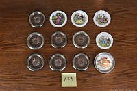 Top view of all 12 coasters arranged in rows. Seven decorative illustrated coasters on top and right, five clear glass coasters with starburst designs in middle and bottom rows.