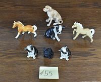 Seven porcelain animal figurines arranged on wooden surface showing dogs and horses