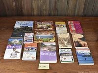Photo showing 13 books arranged on a wooden surface including 11 travel books focused on Scotland, Italy, New Brunswick, Prince Edward Island, and two Penguin Press books.