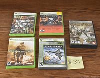 Photo of the lot showing five video games including four Xbox 360 games and one PC game arranged on a wooden surface.