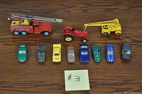 Full view of 10 vintage toy vehicles including 8 cars, 1 tractor, and 1 crane truck on wooden surface.