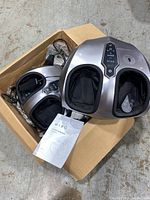 Two Miko foot massagers with power cords and remote controls inside an open cardboard box on a concrete floor.