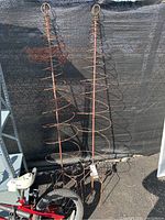 Two tall, rust-colored metal spiral plant supports with circular spirals, standing outdoors against black mesh fabric.