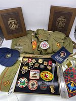 Overview of two Boy Scout uniforms, two blue caps, belt, and framed patch and pin collection.