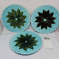 Three Majolica plates placed upright showing turquoise background with green Lily of the Valley leaves and flower details.