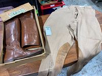 Photo of vintage brown leather equestrian riding boots in box and beige riding pants on table to show overall lot items