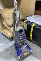 Full view of Hoover SteamVac upright cleaner showing handle, clear water tank, hose, and body of the vacuum standing upright in a storage area.