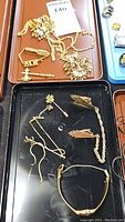 Overhead photo showing two trays of assorted gold-tone jewelry including chains, brooches, and pins