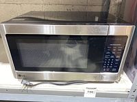 Front view of stainless steel LG microwave oven showing the door, keypad controls, and power cord.