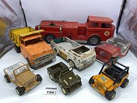 Photo showing all eight vintage metal toy trucks and Jeeps arranged with the fire truck in the back, dump truck and other trucks in front, and three Jeeps
