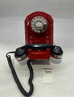 Front view of the red rotary wall phone with black handset and coiled cord.