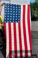 Full view of vintage US flag with 48 stars and 13 stripes showing wrinkles and small hole