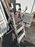 Full view of the folding stepstool ladder standing open outdoors, showing aluminum frame and black plastic top and step platforms.