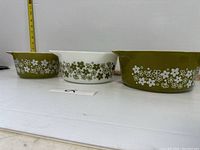 Three vintage green and white Pyrex nesting bowls arranged side by side showing front floral patterns