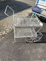 Side perspective showing white metal frame, bottle holders, mesh shelves, decorative wheels, and handle.