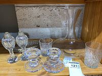 Overall display of two candlesticks, salt and pepper shakers, decanter, relish dish, and glasses on a wooden shelf.