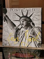 Framed giclee art print showing close-up of Statue of Liberty and 'New York' in yellow script with vintage postcard background.