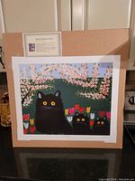 Photograph showing the entire lithograph with three black cats amidst colorful flowers and floral branches, unframed and mounted on cardboard.