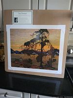 Photo showing the unframed lithograph 'The Jack Pine' by Tom Thomson mounted on a brown backing board, with artist information label visible on top left.