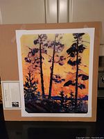 Full view of lithograph taped on cardboard showing pine tree silhouettes at sunset in vibrant orange and yellow colors.