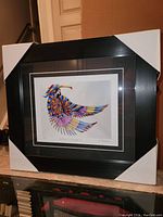 Framed fine art print with protective corner covers showing full piece including matting and black frame.