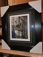 Full view of professionally framed fine art print with protective corner guards on black frame to show lot condition and style.