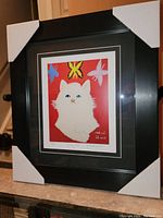 Framed print showing white 'Grumpy Cat' with blue eyes, butterflies on red background, black frame with corner guards.
