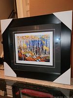 Framed fine art print showing woods with birch trees and vibrant fall colors, black frame with protective corners attached.