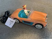 Side view of orange convertible Barbie car with Barbie figure, power cord and catalog card.