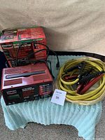 Battery charger alongside jumper cables coiled on a towel.