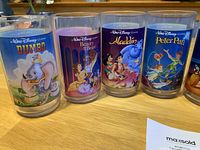 Photo showing four cups featuring Dumbo, Beauty and the Beast, Aladdin, and Peter Pan with colorful Disney character prints.