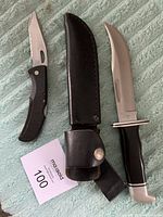 Two knives displayed including Buck 119 fixed blade with sheath and Gerber folding knife with serrated blade.