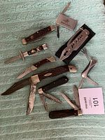 All seven cutting tools arranged on a light blue textured cloth showing folding knives and multi-tools